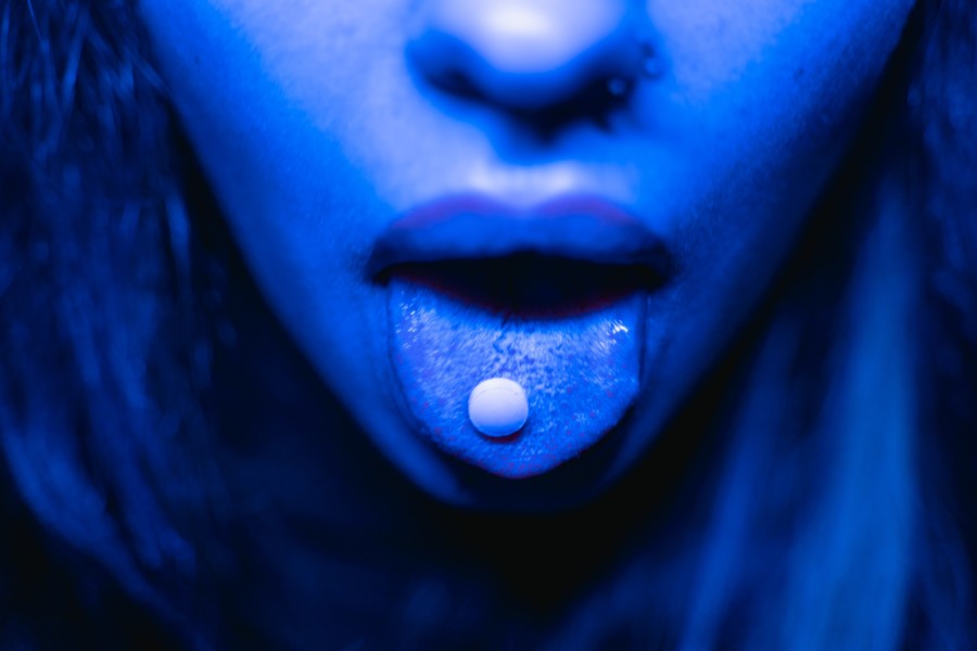 Nariz y boca con la lengua afuera y en ella una pastilla. Foto oscura, ambiente perturbador.