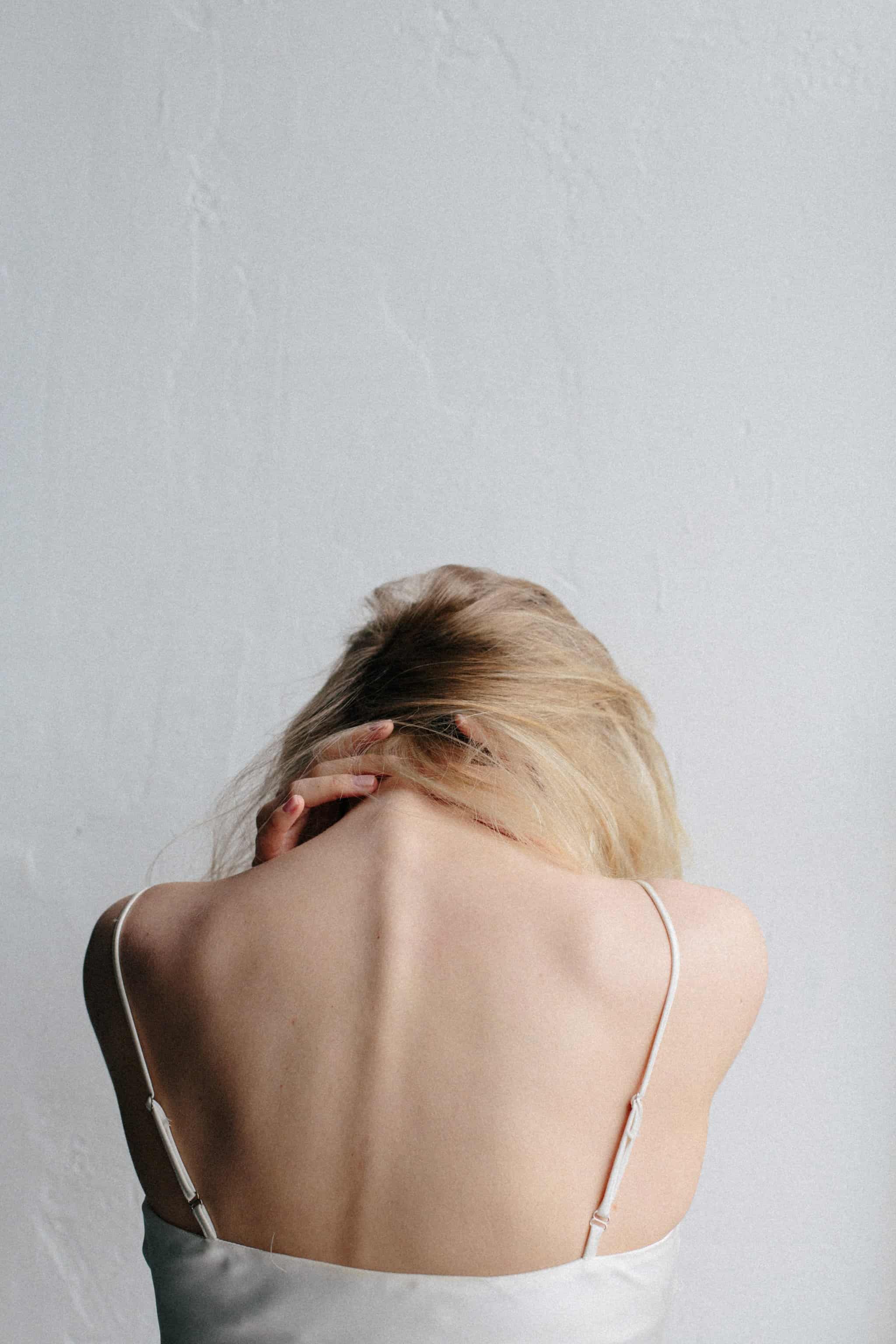 Mujer rubia de espaldas agarr&aacute;ndose el cuello en un gesto de dolor